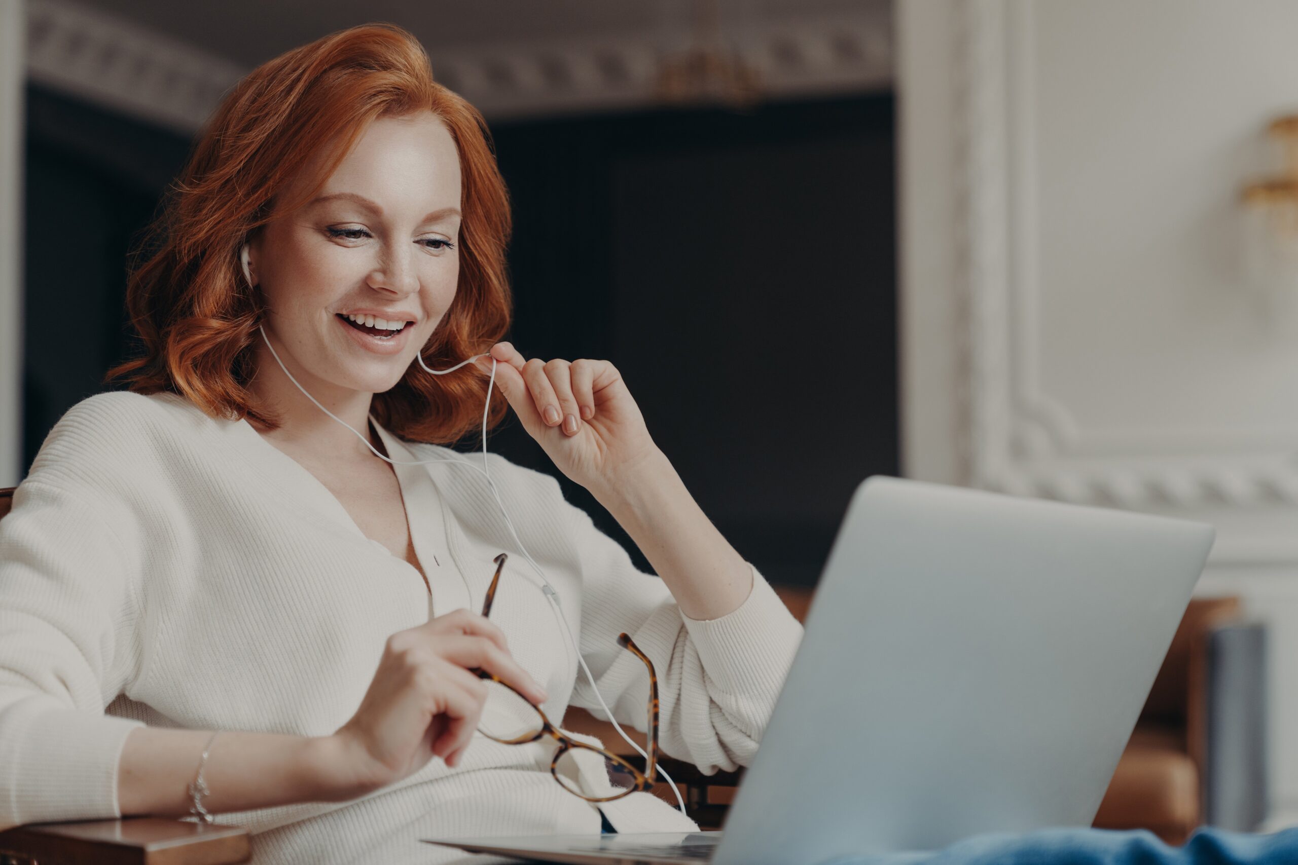 Satisfied happy foxy successful woman has video conference, uses modern laptop computer and earphones, browses data and works on remote project, poses in modern apartment, watches online webinar happy foxy successful woman has video conference 2022 11 07 23 31 50 utc scaled